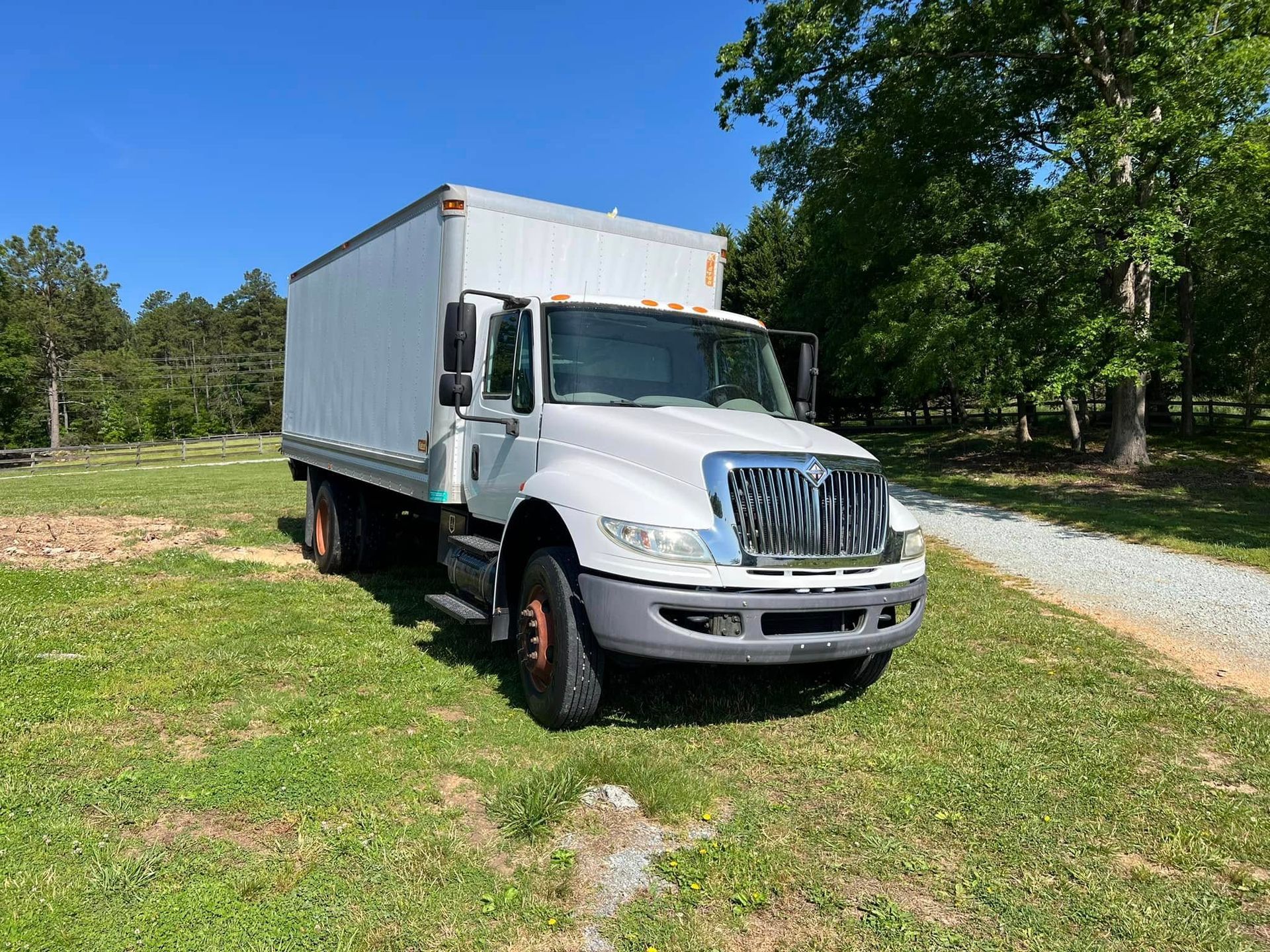White box truck parked on grass beside a gravel drive under a clear blue sky