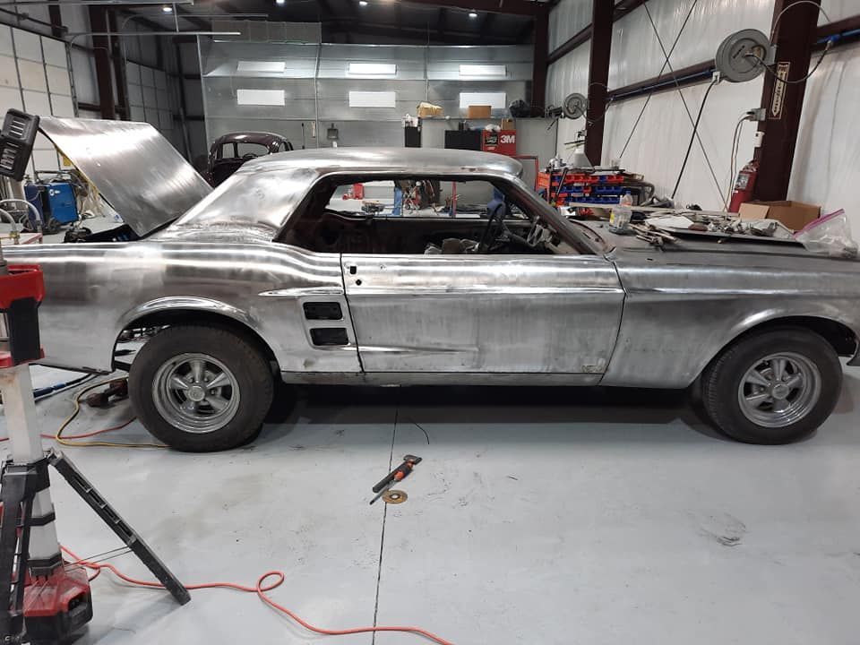 Silver classic car under restoration in a garage, with primer patches and tools on the floor