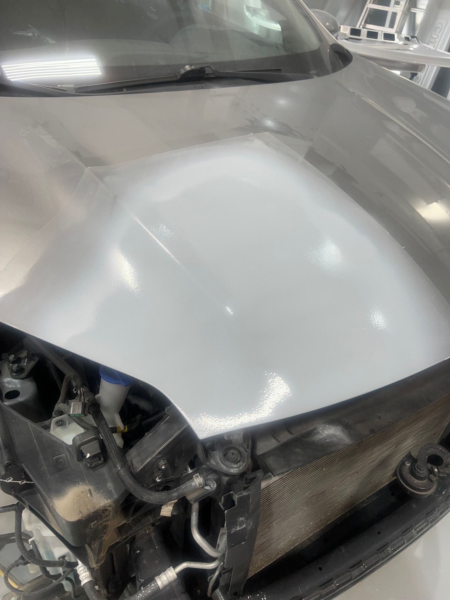 Damaged silver car front end with broken bumper, exposed internal parts, and scuffed hood