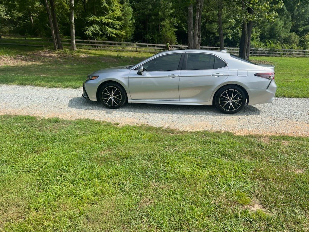 Silver sedan parked on a gravel drive beside a grassy lawn and trees