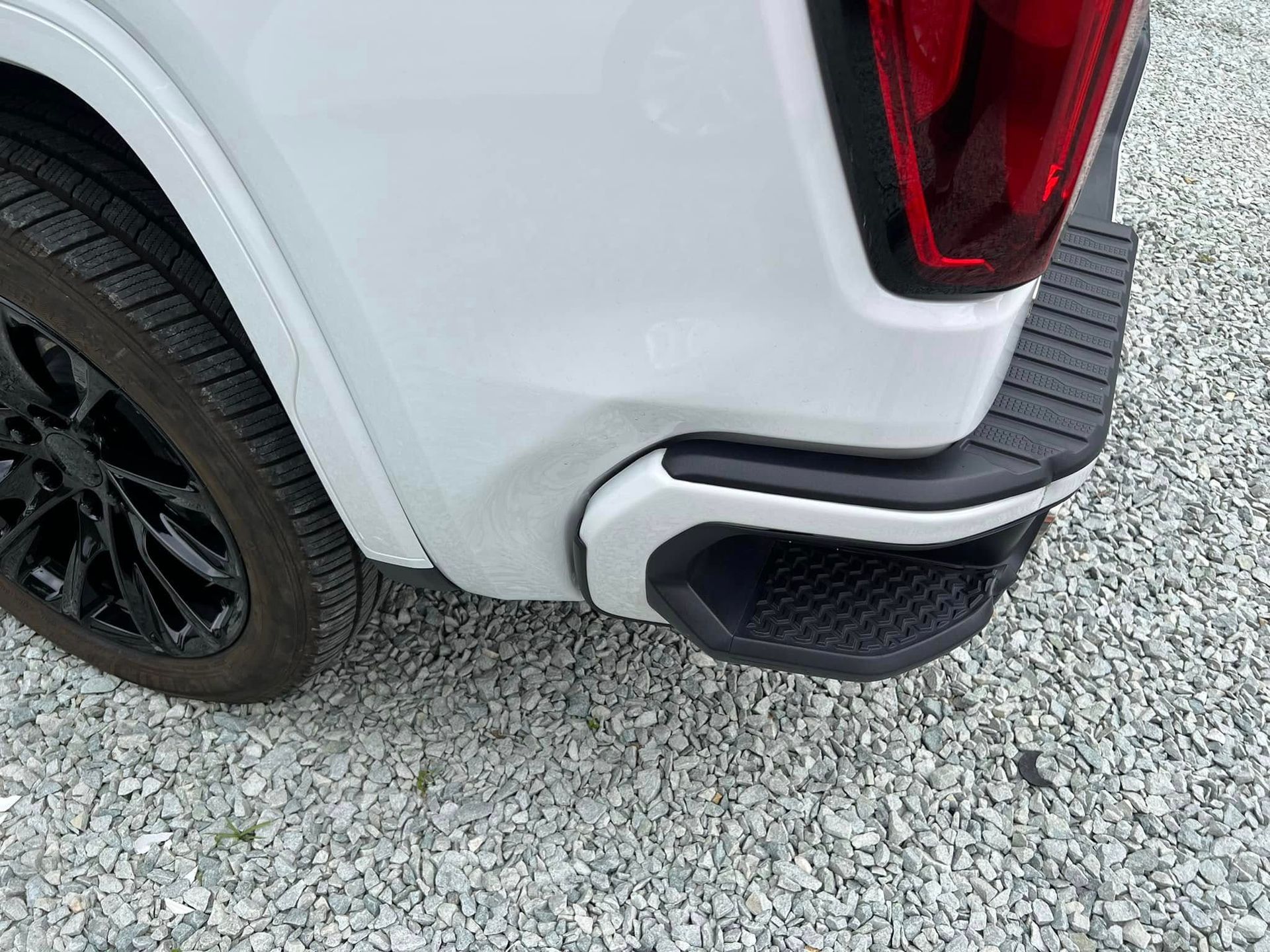 Rear corner of a white SUV with black trim and tire on a gravel surface