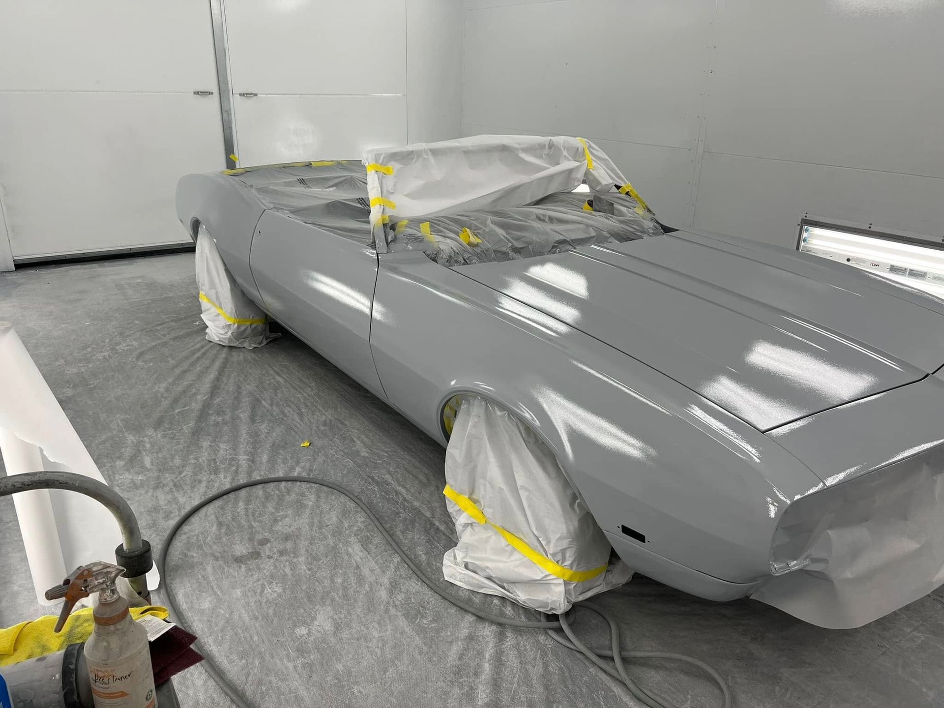 Gray car body in a paint booth, masked with tape and paper, awaiting paint.