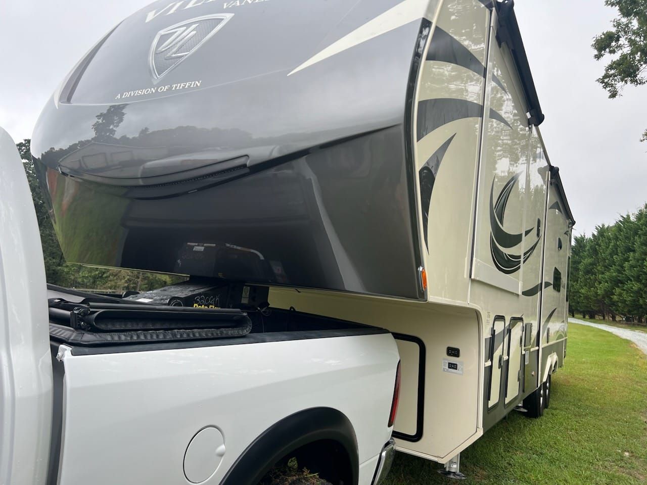 White luxury motorhome parked on grass, with a black-tinted front cap and curved side graphics.