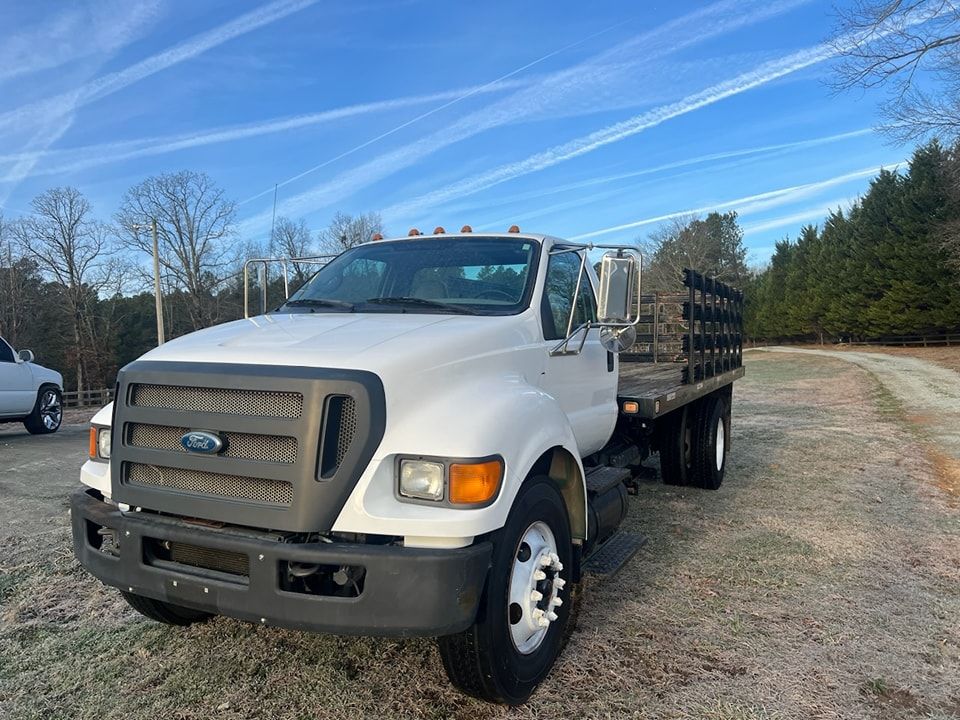 White flatbed truck parked on gravel under a blue sky with wispy clouds.
