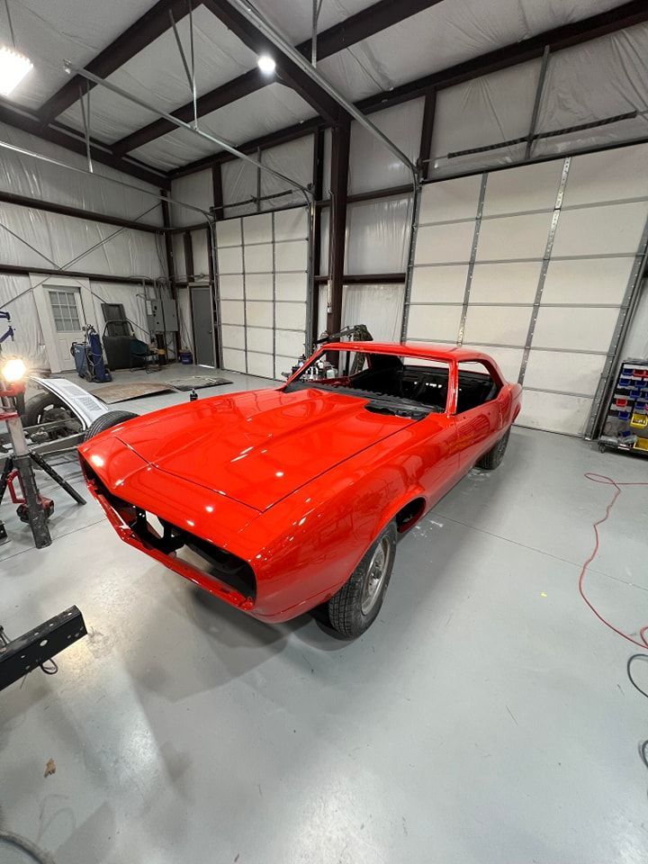 Red classic muscle car in a garage with a lifted front end and bright workshop lighting