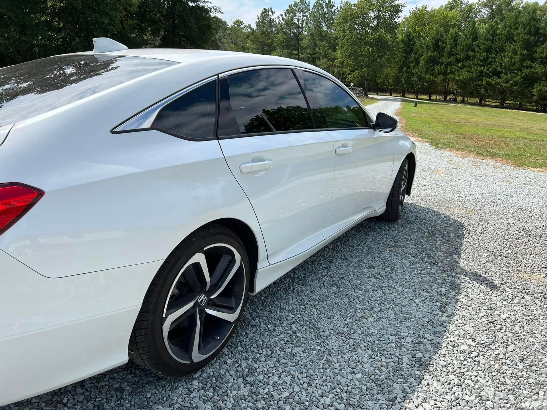 White sedan parked on a gravel driveway beside a grassy yard and trees