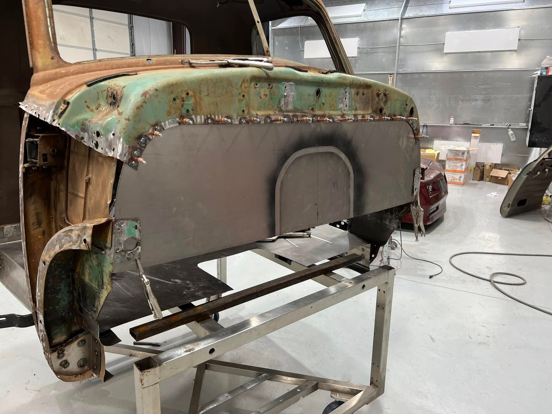 Rusty green car body shell on a metal stand in a workshop, with exposed metal and unfinished surfaces
