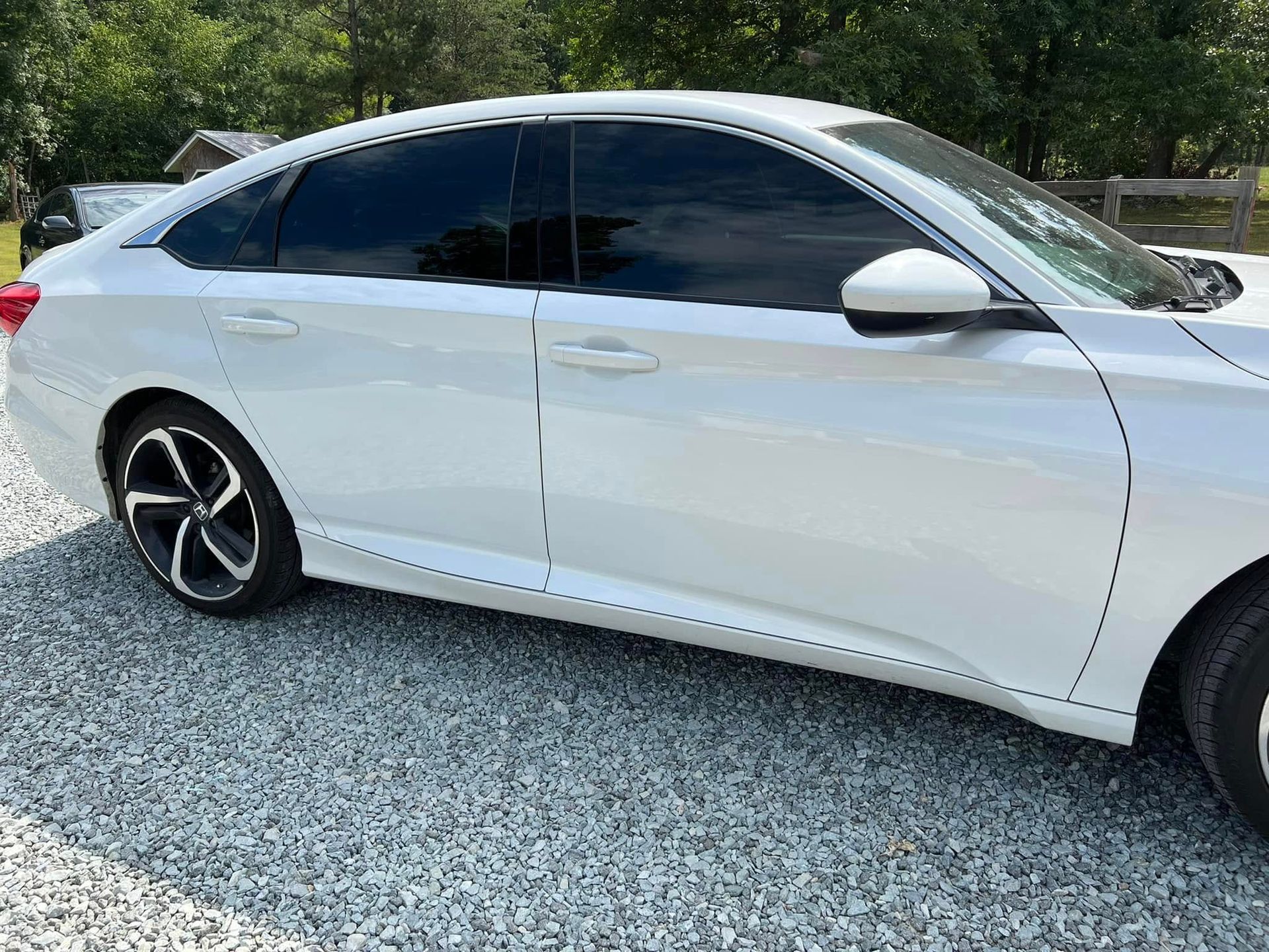 White sedan parked on gravel with tinted windows and trees in the background
