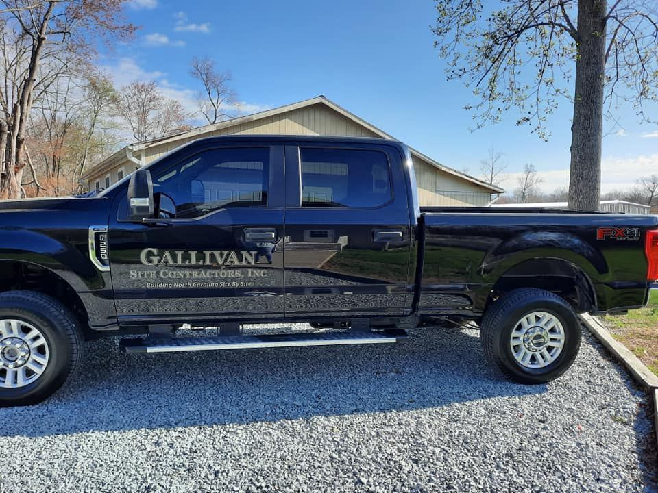 Black pickup truck with GALLIVAN branding parked on a gravel driveway by a house.