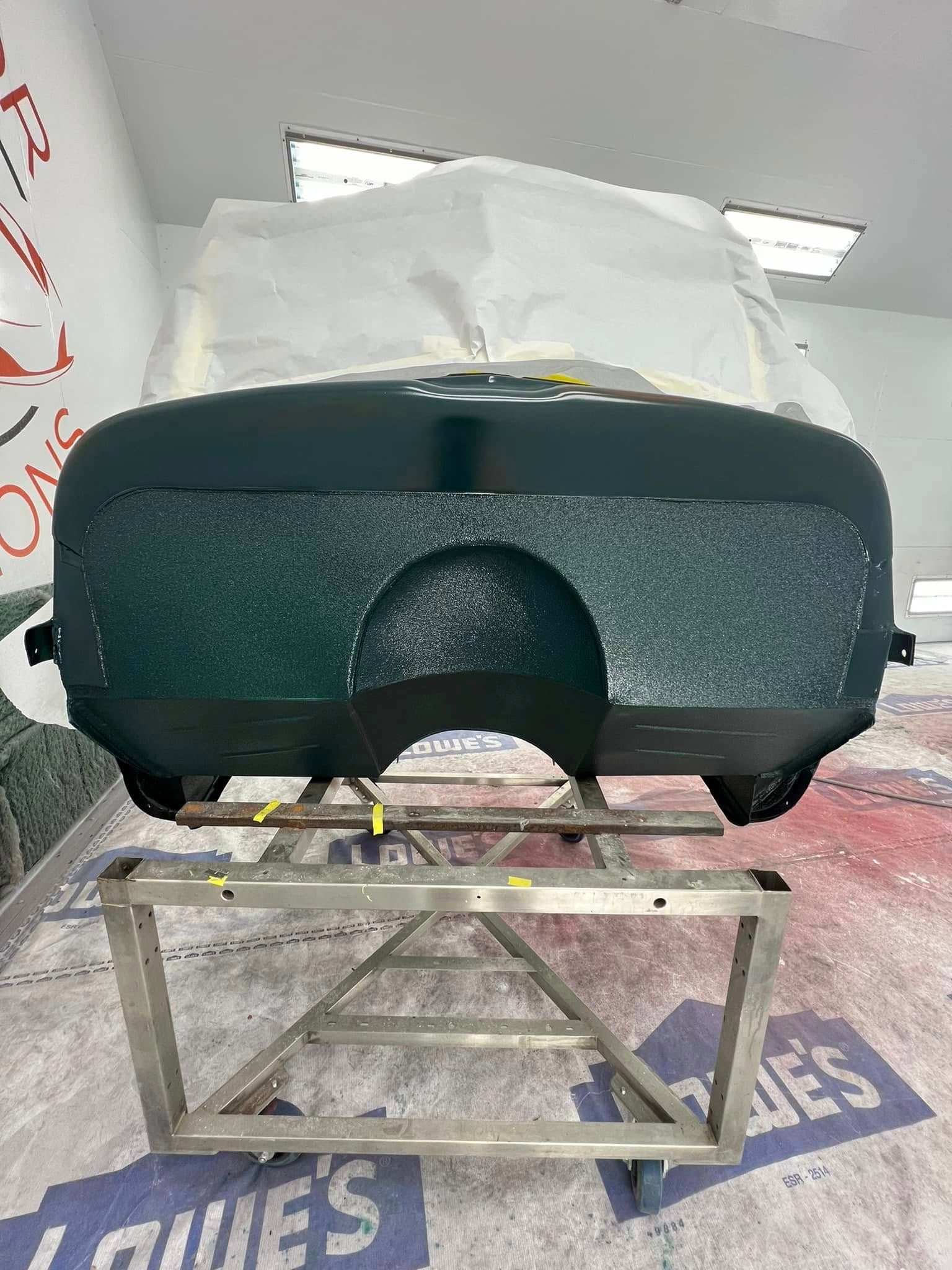 Dark green car front panel on a metal stand in a workshop, covered partly with protective plastic