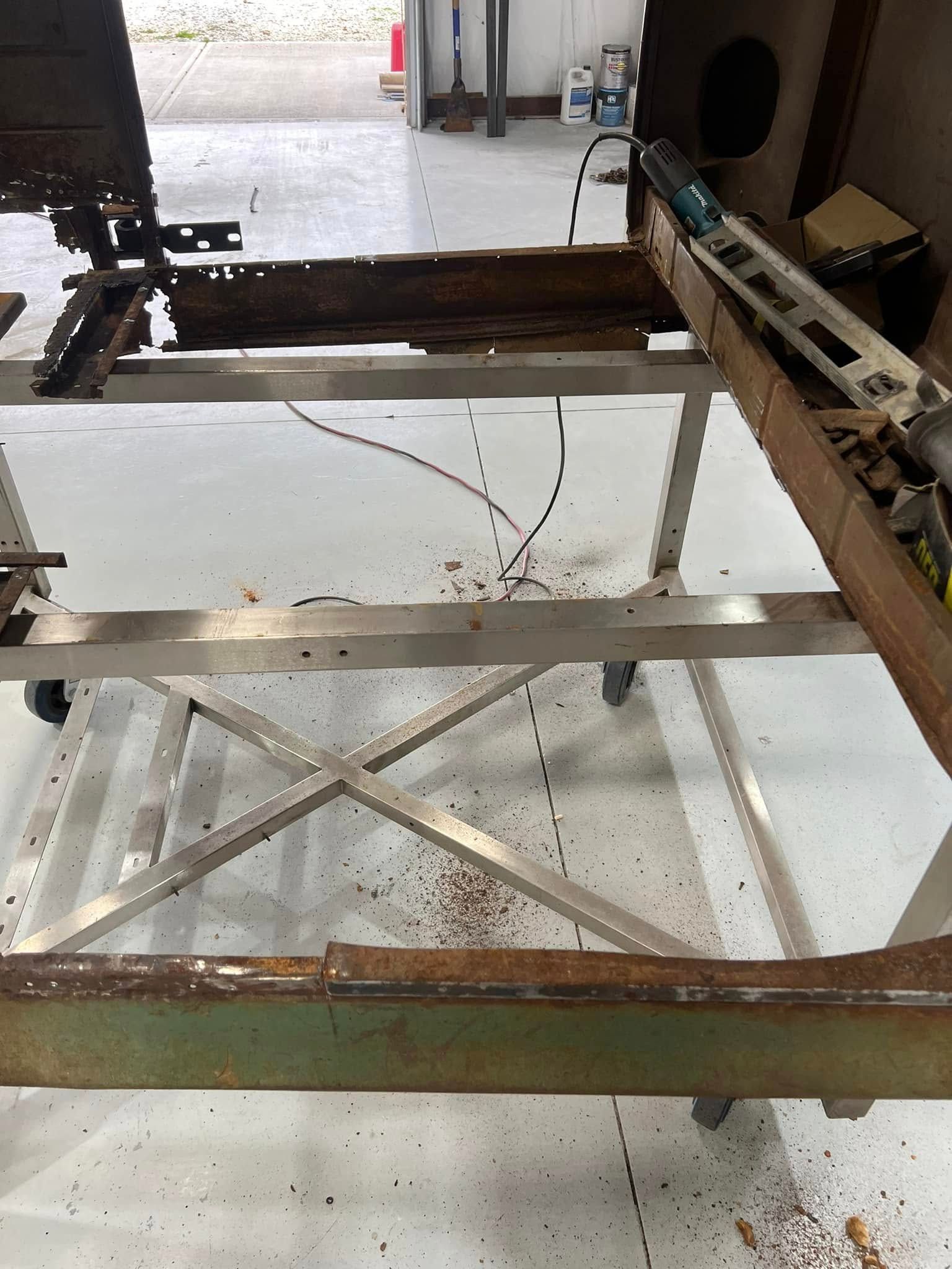 Old metal frame or workbench with rust and cross bracing, viewed in a workshop or garage.