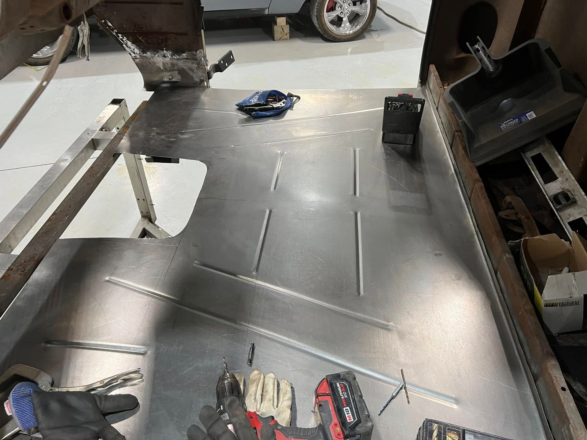 Metal sheet in a workshop, with tools and gloves laid out on top and a vehicle visible in the background.