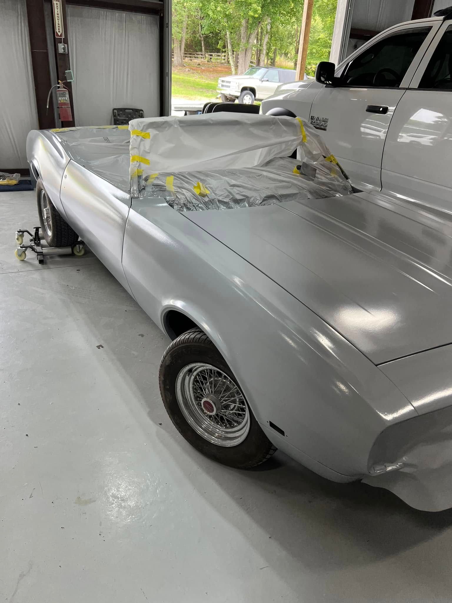 Silver vintage car undergoing bodywork inside a garage, covered with masking tape and paper