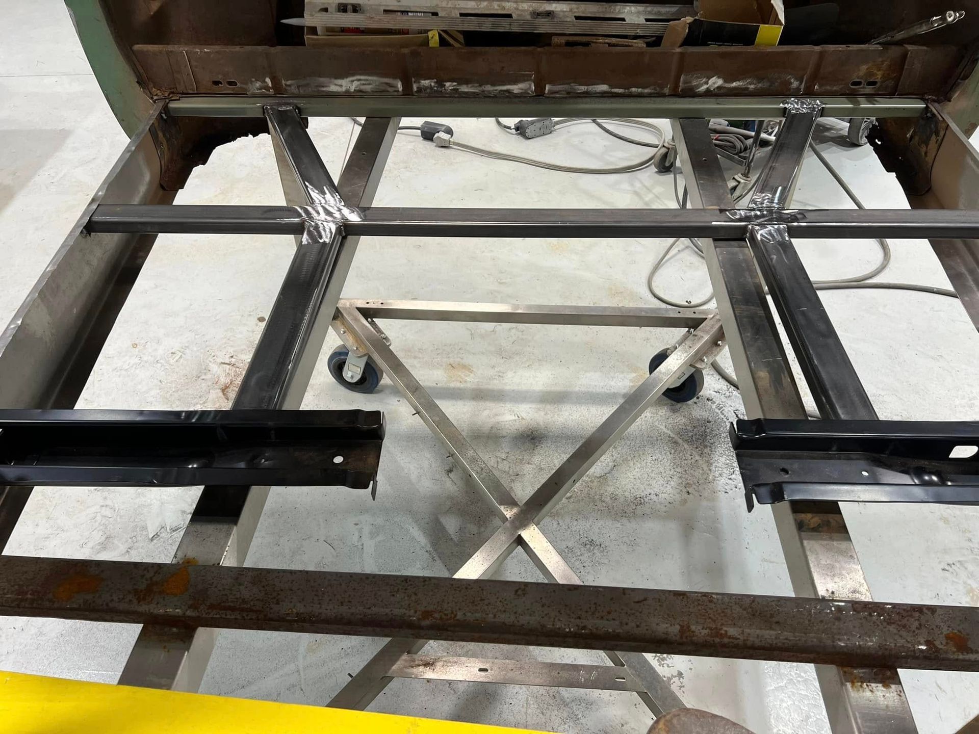 Metal frame of a disassembled table or cart on a concrete floor, with wheels and crossbars visible
