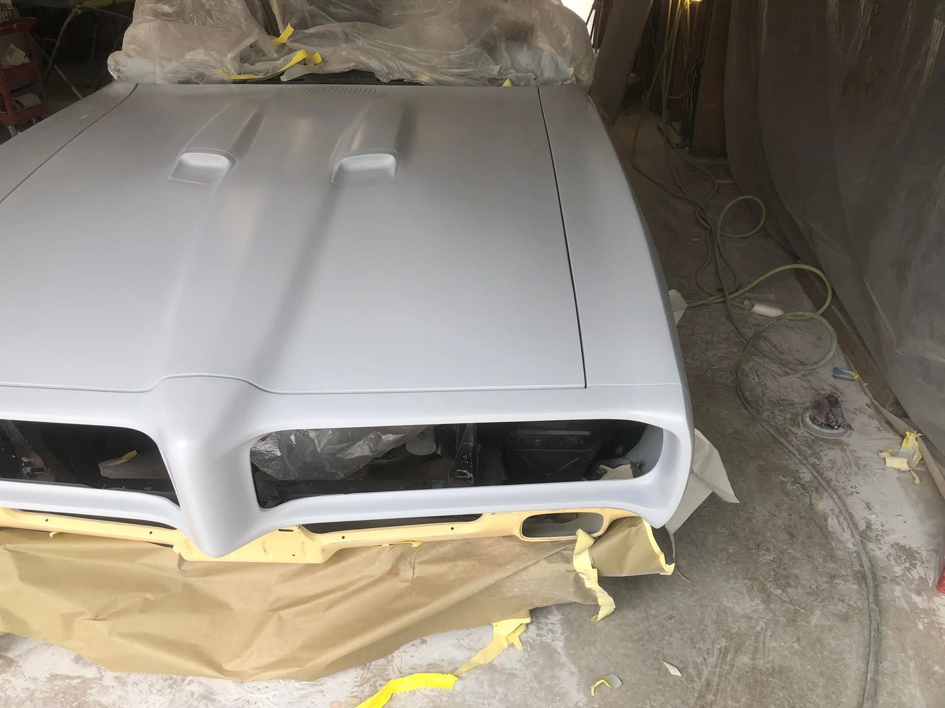 White car hood and front end in a workshop, masked with paper and ready for paint.