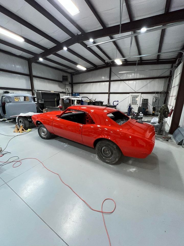 Red sports car in a workshop garage with a gray SUV and tools in the background