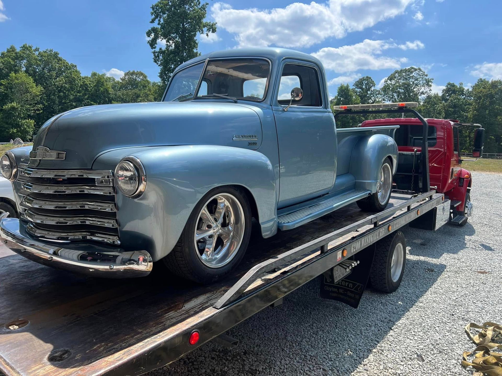 Blue vintage pickup truck on a tow trailer, parked outdoors on a sunny day.