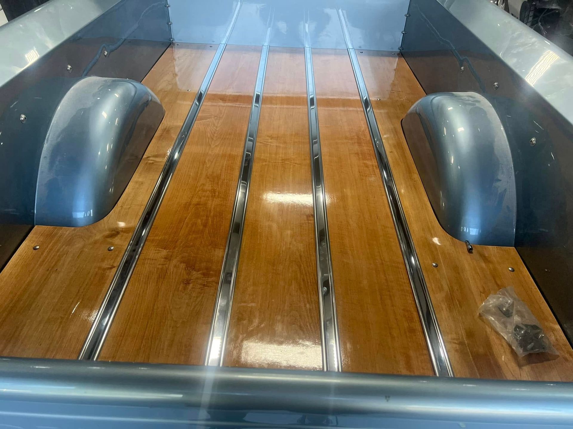 Wooden truck bed with two black wheel wells and shiny metal trim under bright light