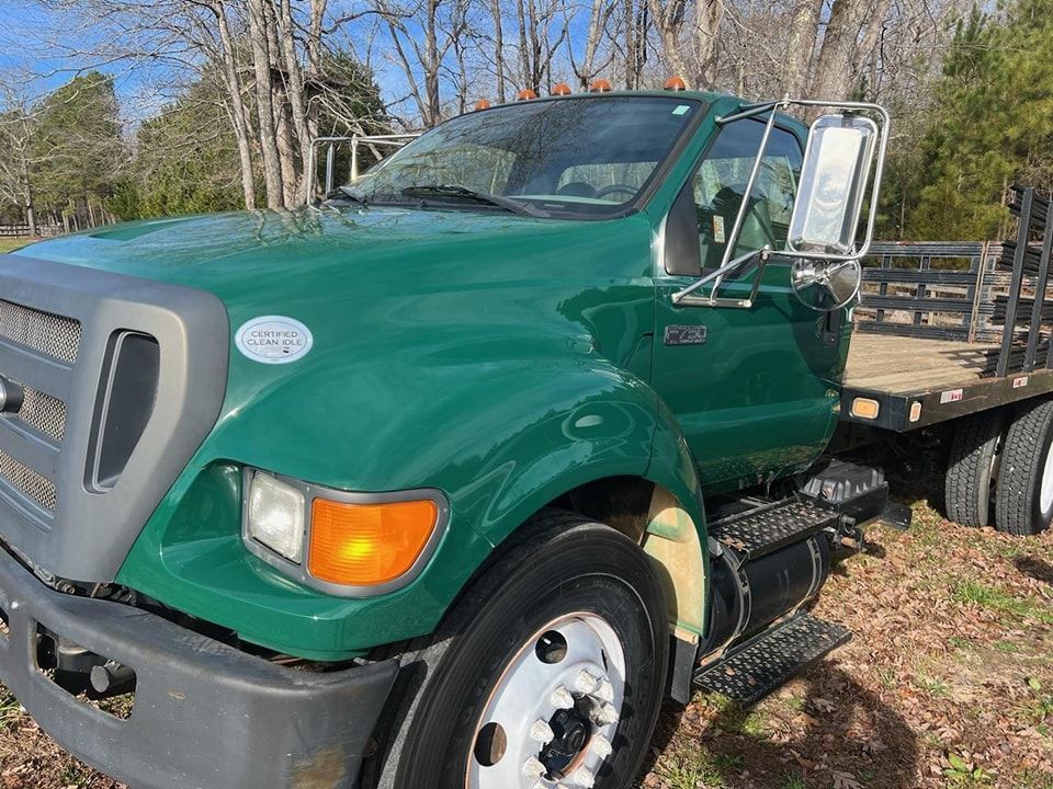 Green flatbed truck parked outdoors with open door and trees in the background