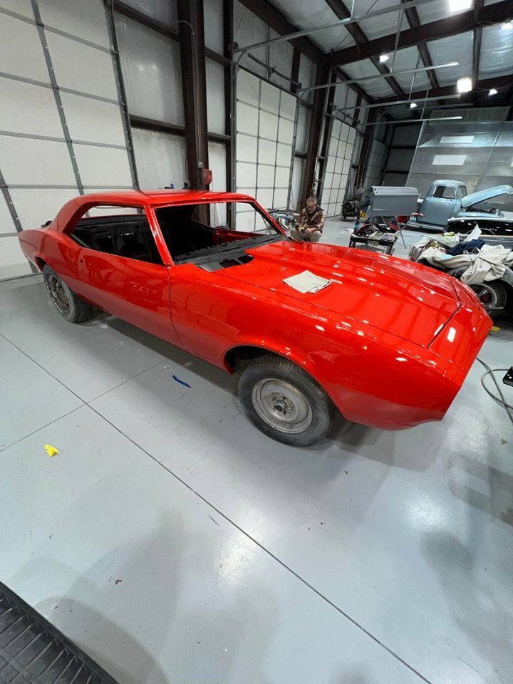 Red classic car in a garage with other vehicles nearby