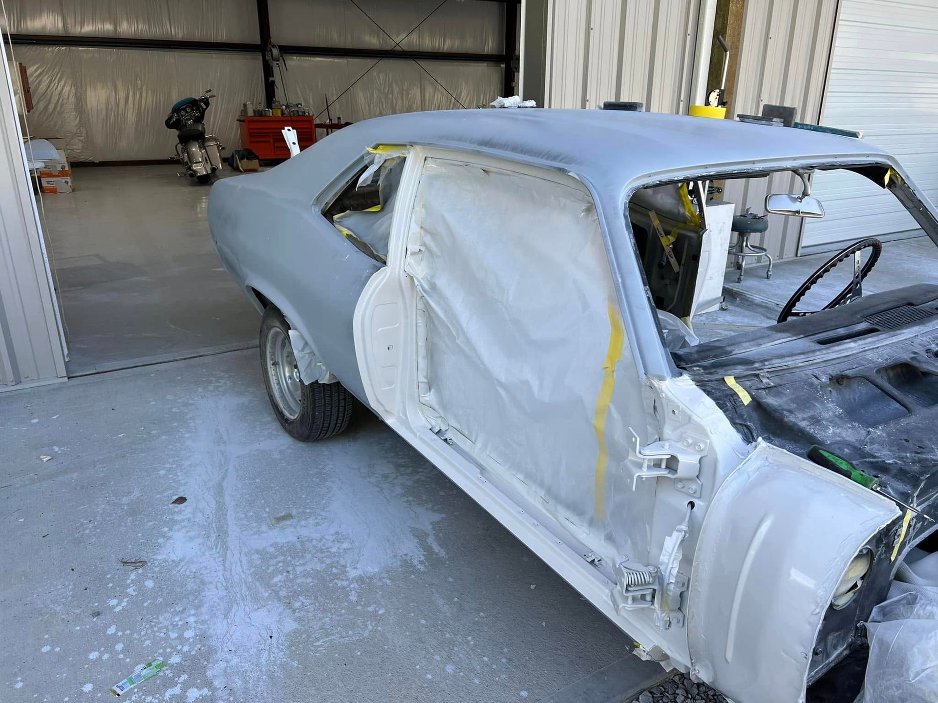 Primer-coated classic car in a workshop, with doors removed and front end partially disassembled.