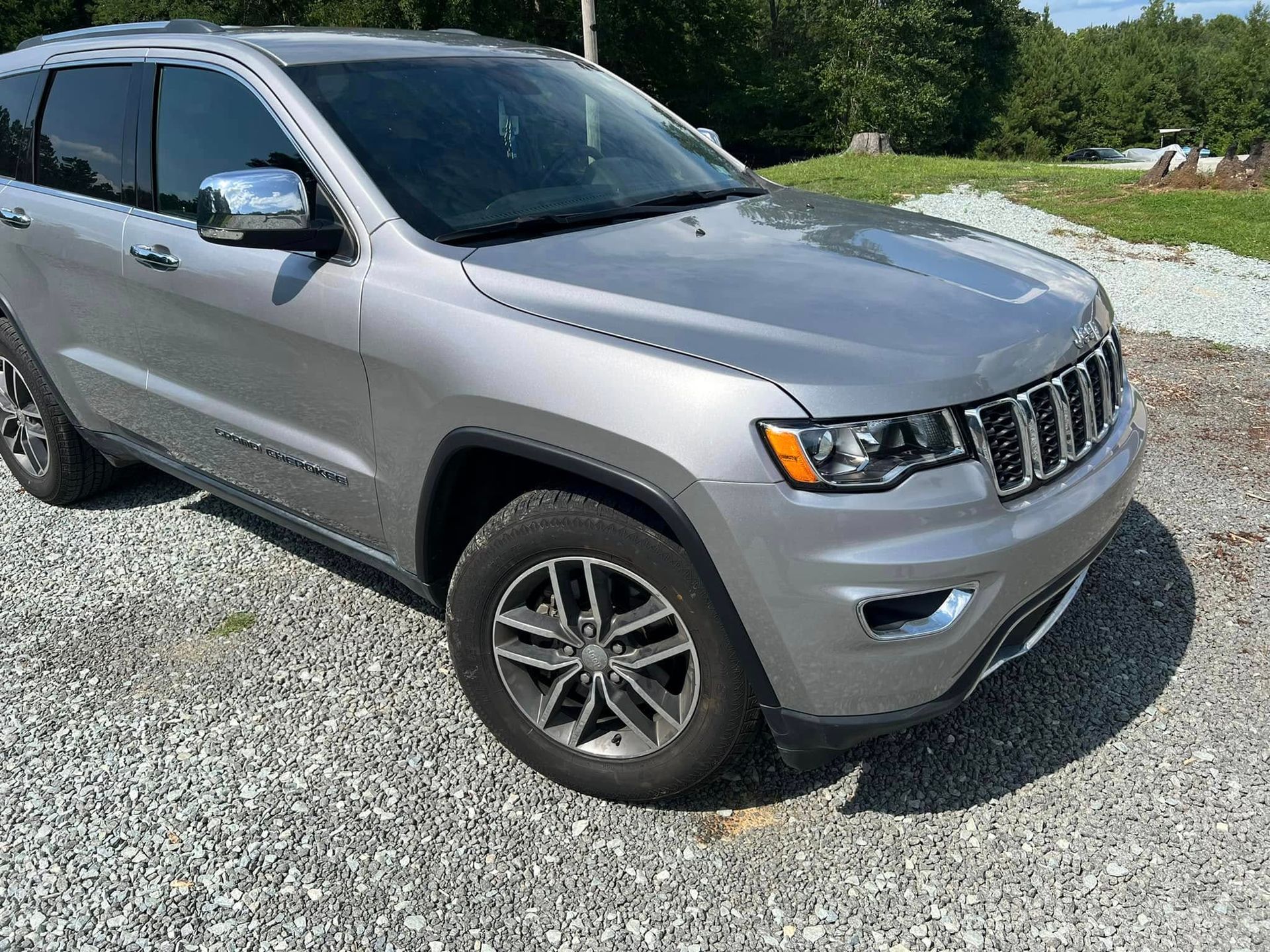 Silver Jeep SUV parked on a gravel lot near greenery on a sunny day