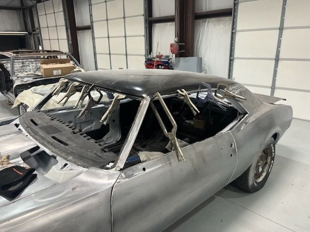 Damaged silver classic car with crushed roof inside a warehouse garage