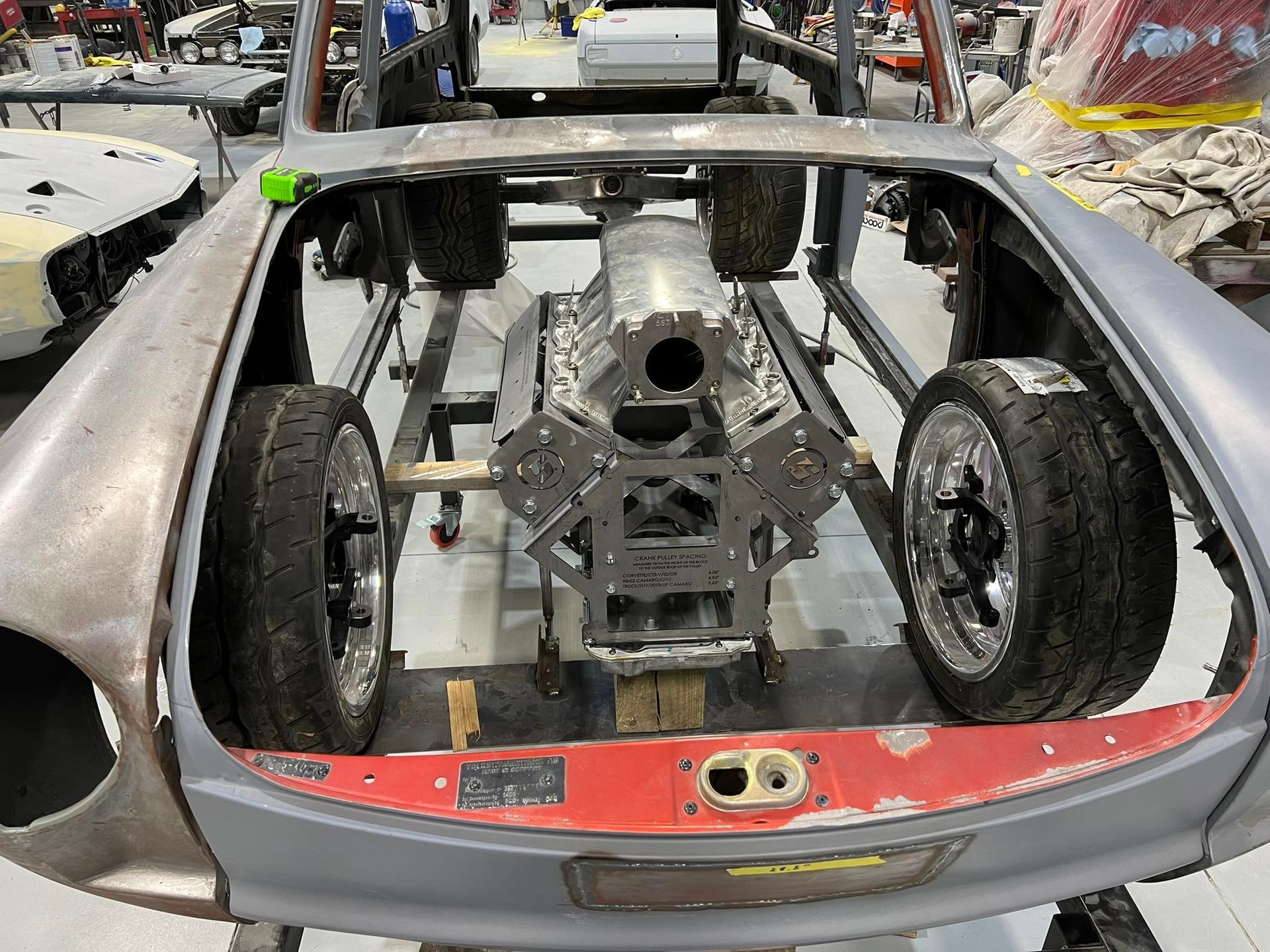Silver sports car shell with exposed engine and interior in a workshop, rear view