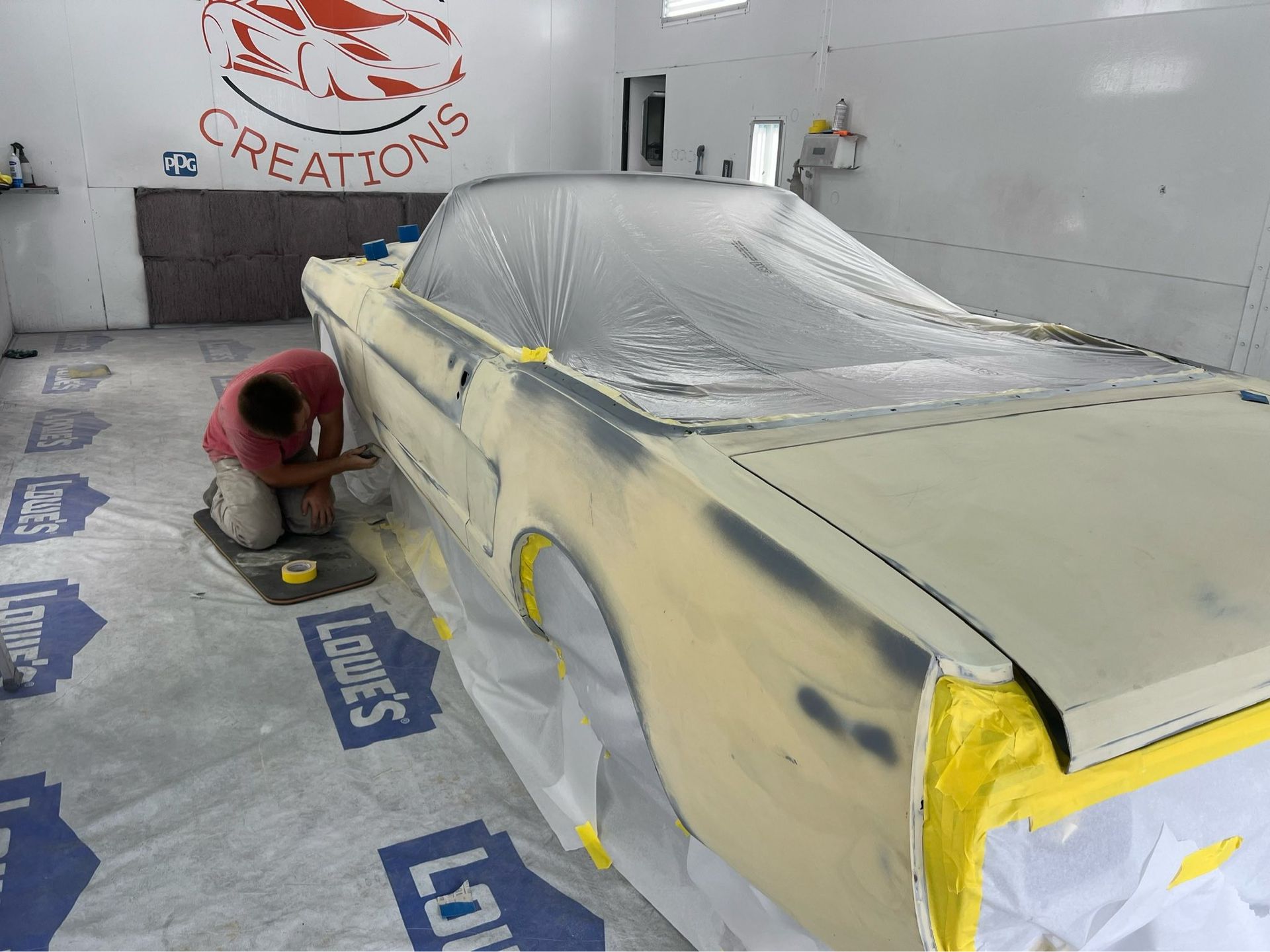 Person sanding a masked car body in a paint booth