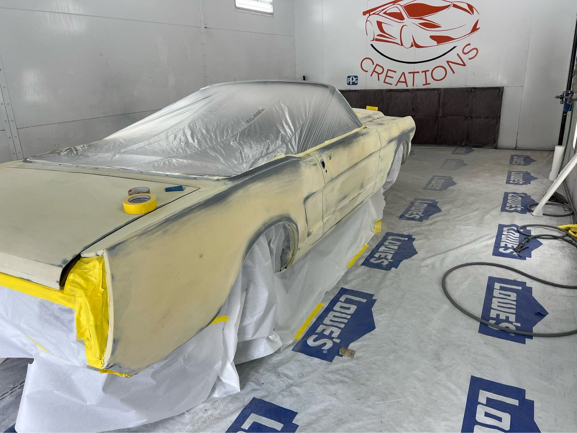 Car under repair, covered in masking paper and plastic in a body shop spray booth