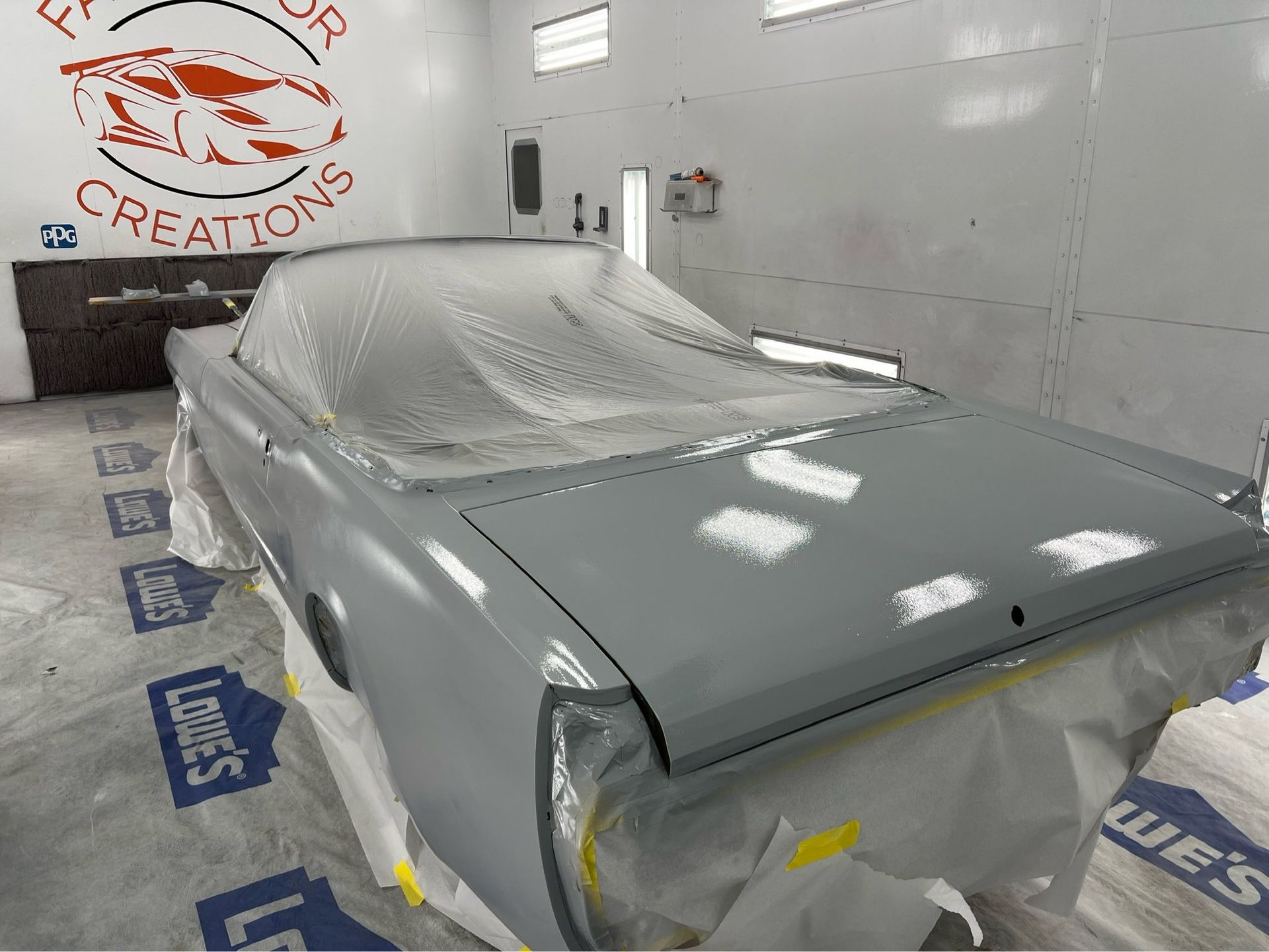 Gray car in an auto body shop, covered in masking paper and plastic, with fresh paint prep visible.
