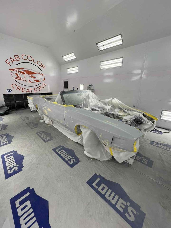 Car wrapped in white plastic inside a paint booth with Lowes floor logos and sprayed walls
