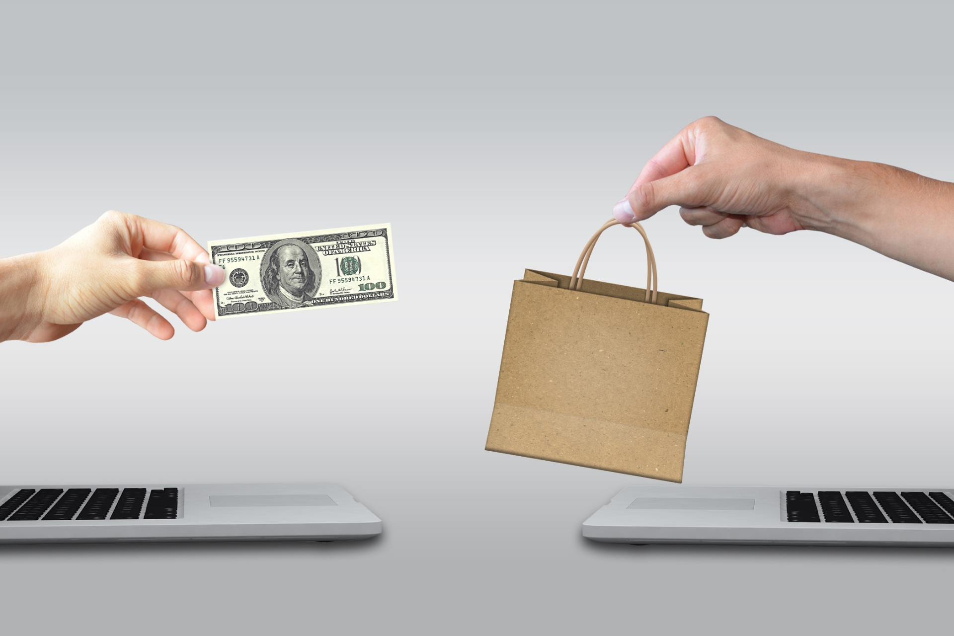Uma pessoa segura uma nota de dólar e uma sacola de compras entre dois laptops.