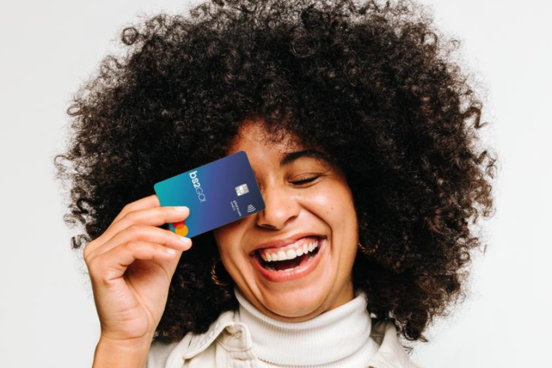 Uma mulher com cabelo afro sorri enquanto segura um cartão de crédito na frente do rosto.