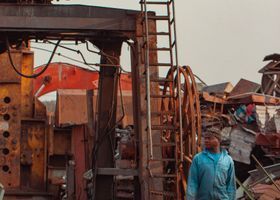 Desguace industrial con una máquina oxidada y una persona con una camisa azul de pie cerca.