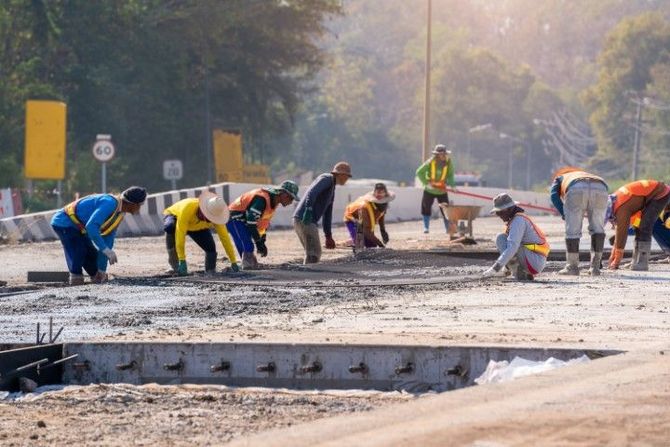 Workers paving a road, bent over smoothing wet concrete in an outdoor construction site.