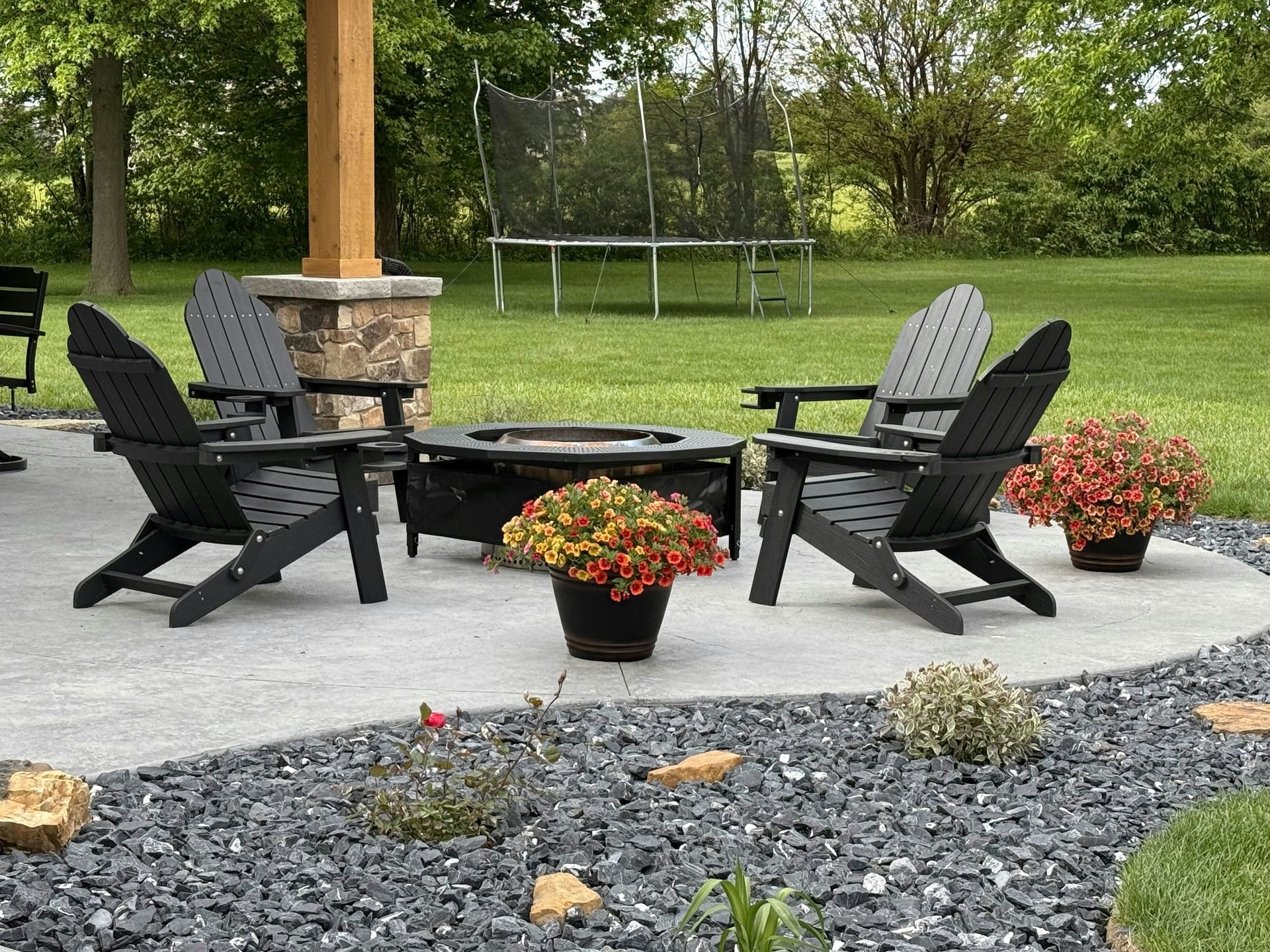 Outdoor patio with black chairs around a fire pit, framed by potted flowers and a green lawn.