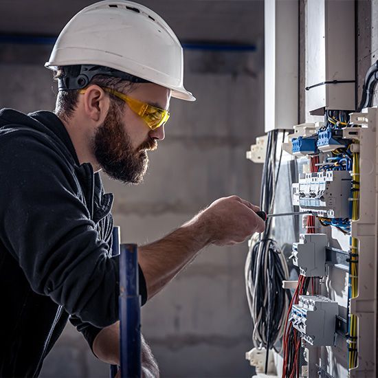 A male electrician works in a switchboard with an electrical connecting cable.