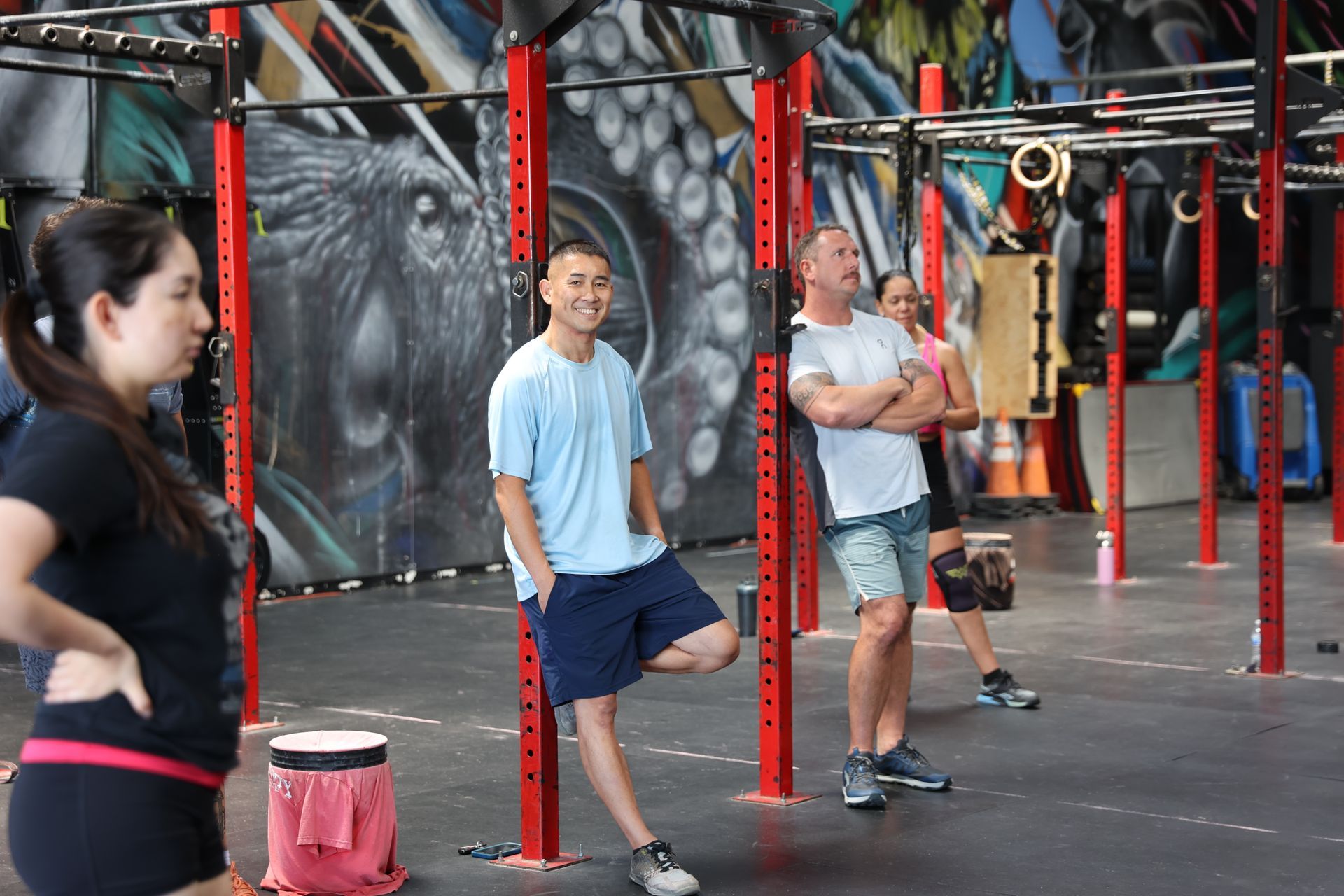 People exercising in a gym with red pull-up rigs and hanging straps at CrossFit ATR in San Diego.