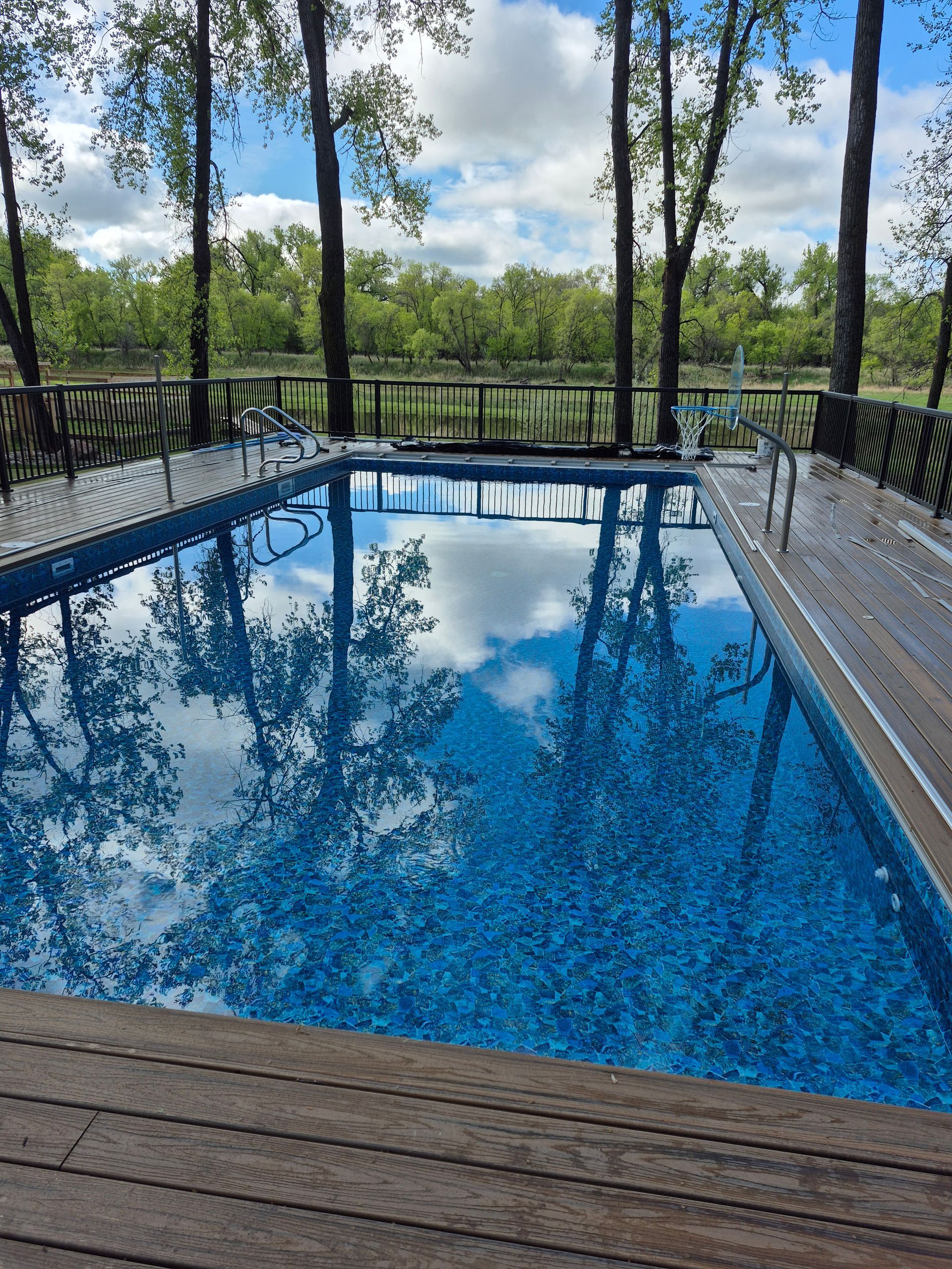 A rectangular pool with clear water, lounge chairs, and a house in the background on a sunny day.