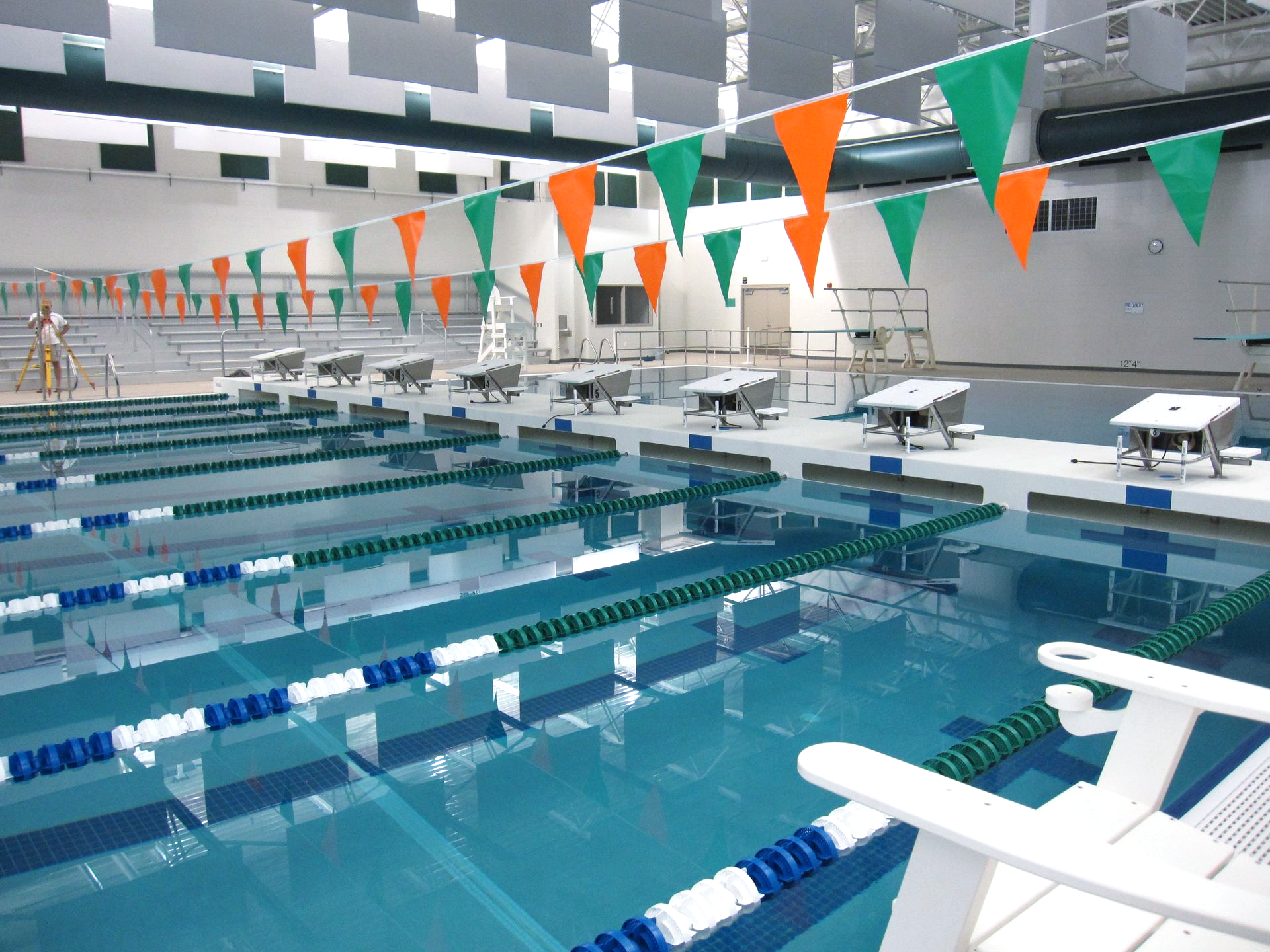 Indoor swimming pool, lanes marked with blue and white, green and orange flags, white starting blocks.