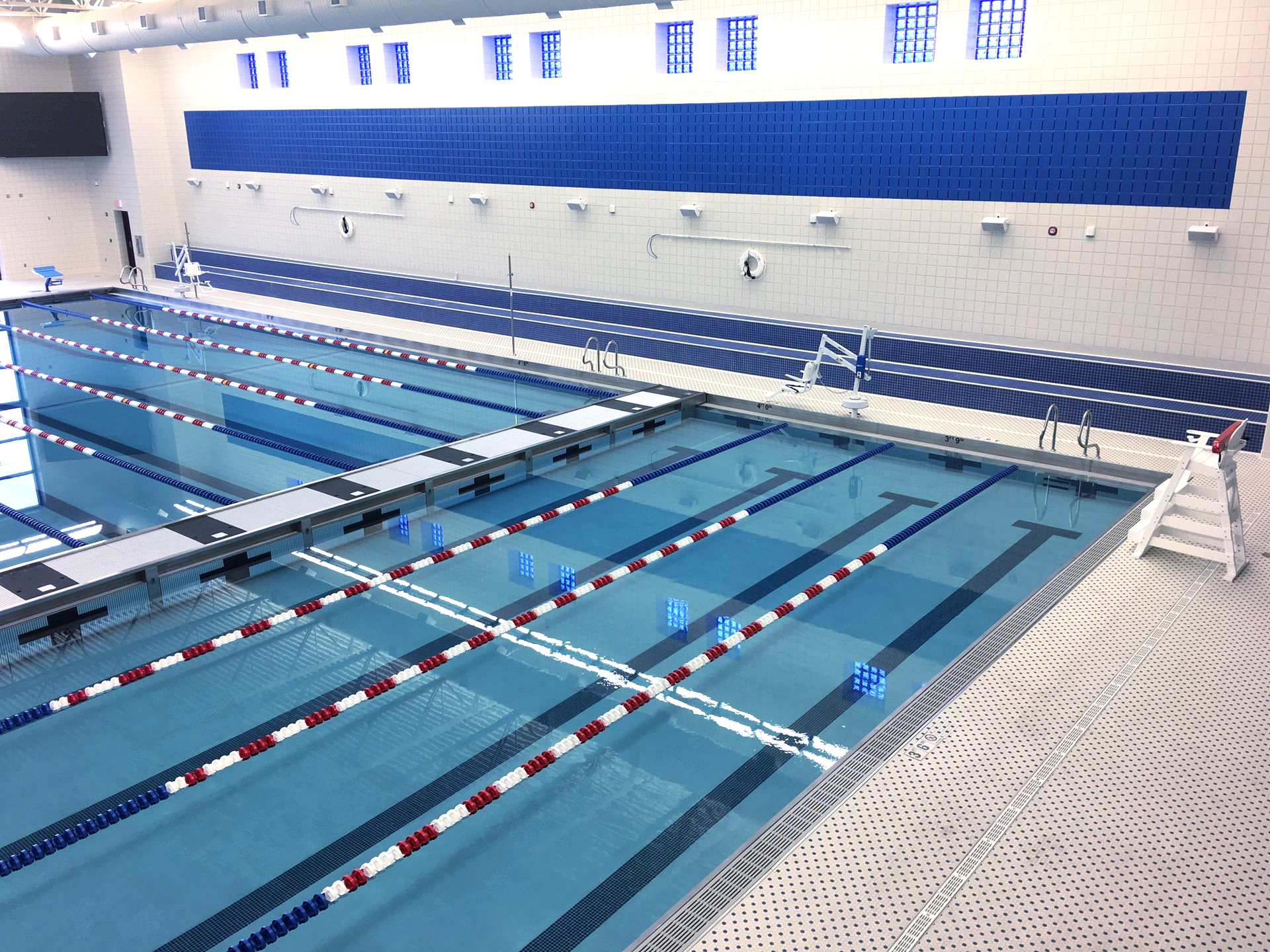 Indoor swimming pool with lanes marked by blue and red lines; white walls and blue trim.
