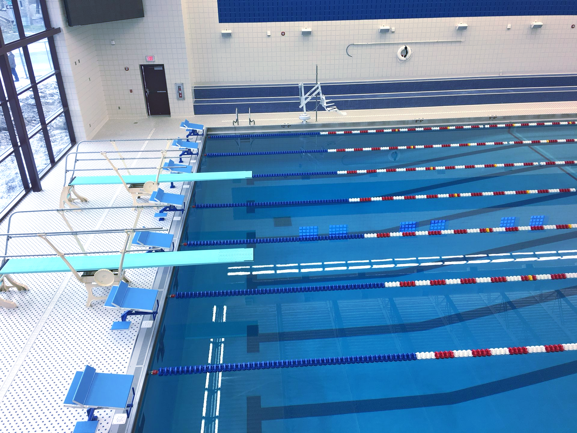 Indoor swimming pool with diving boards and lane markers. Blue water, white tiles, and blue and white lane lines.