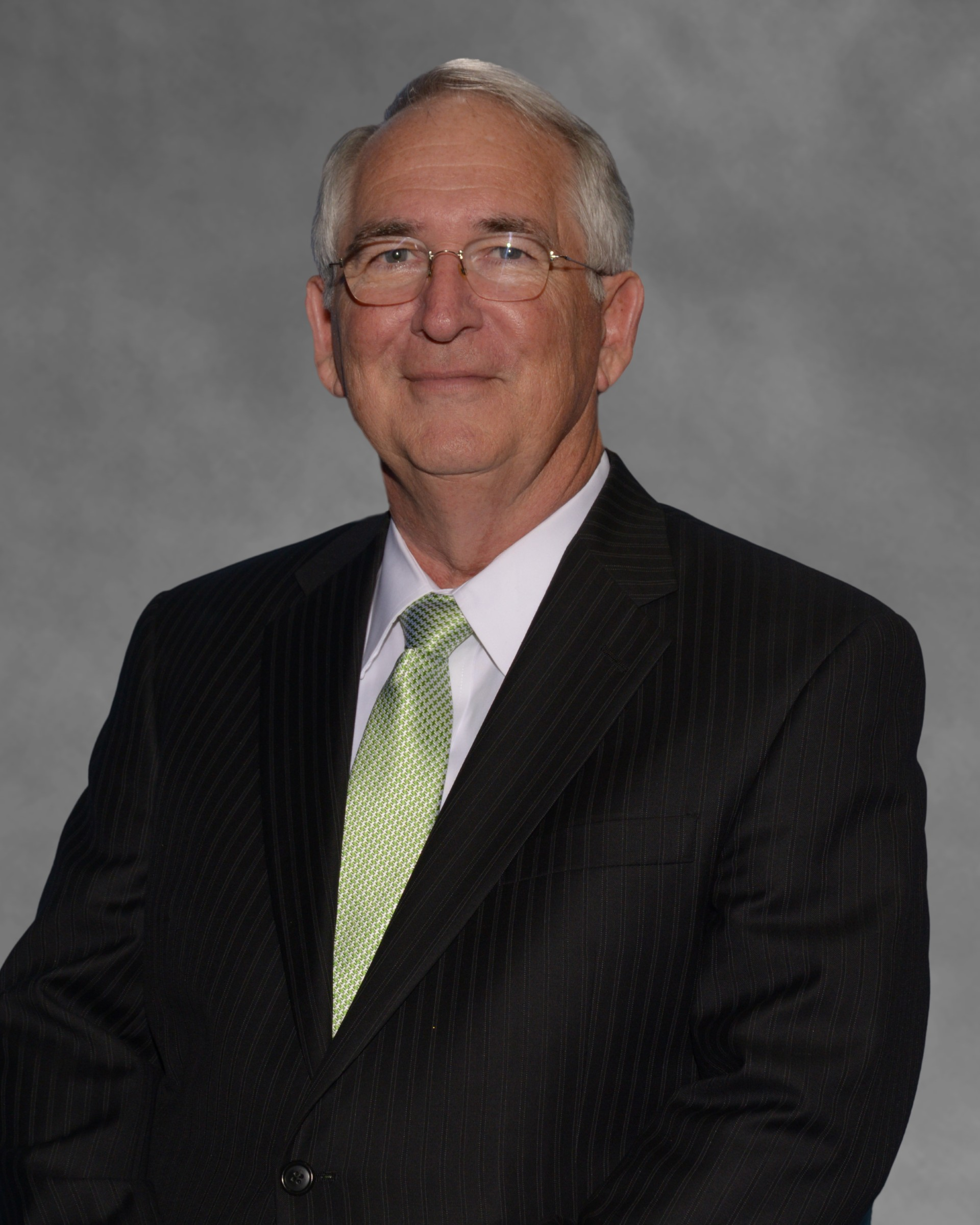Portrait of a man in a dark suit, white shirt, and light green tie against a gray backdrop