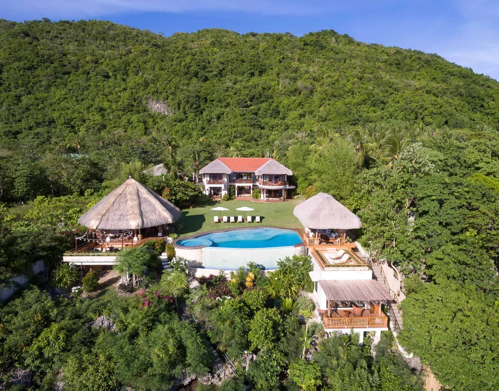 Luxury villa with pool nestled on a hillside overlooking lush green landscape.