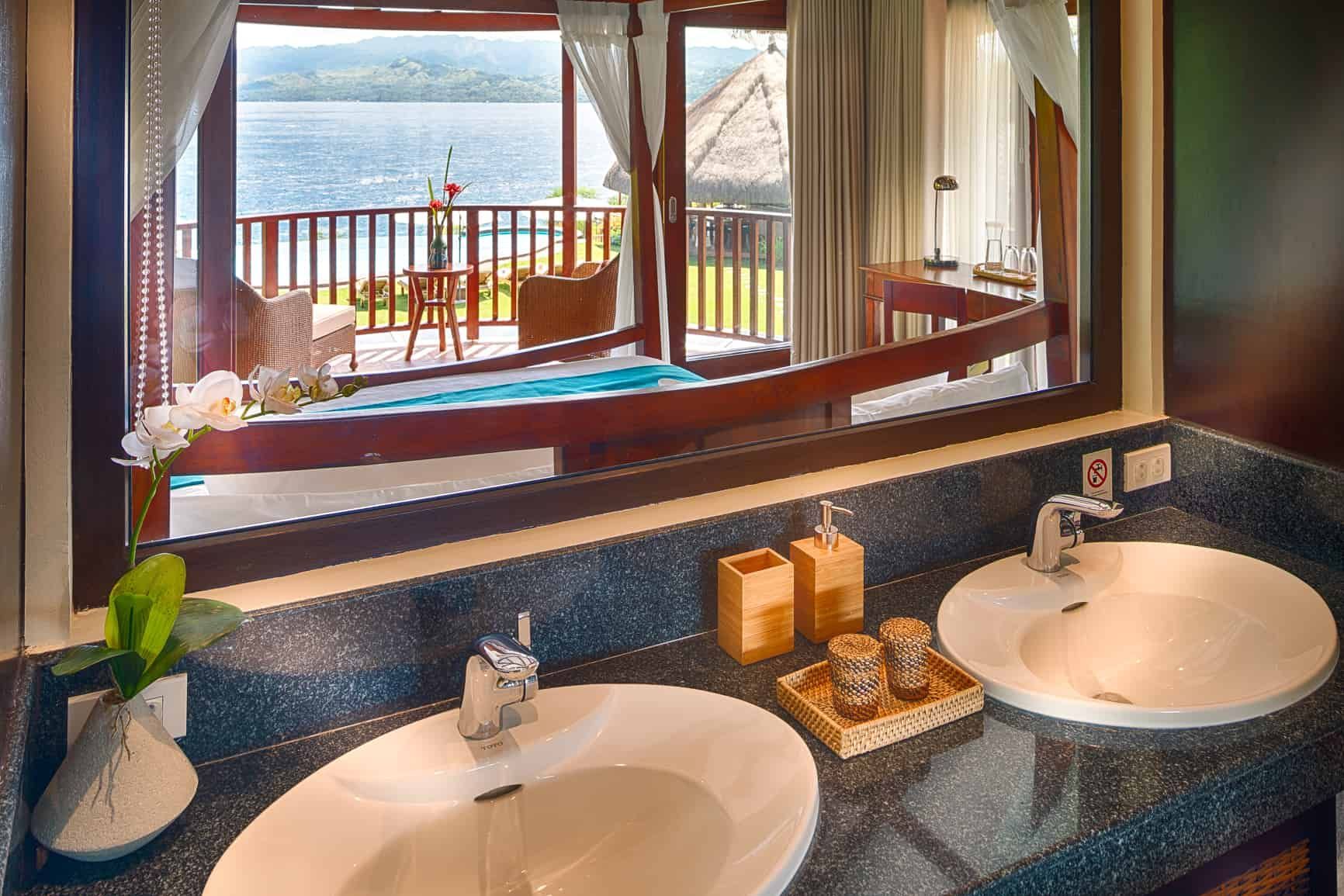 Bathroom with dual sinks, marble countertop, and a mirror reflecting a balcony with ocean view.