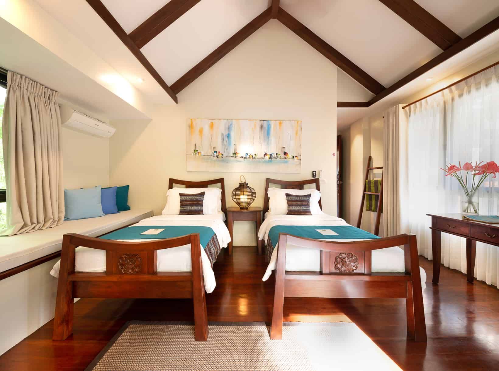Twin beds in a bedroom with wooden furniture, natural light, and a window seat.