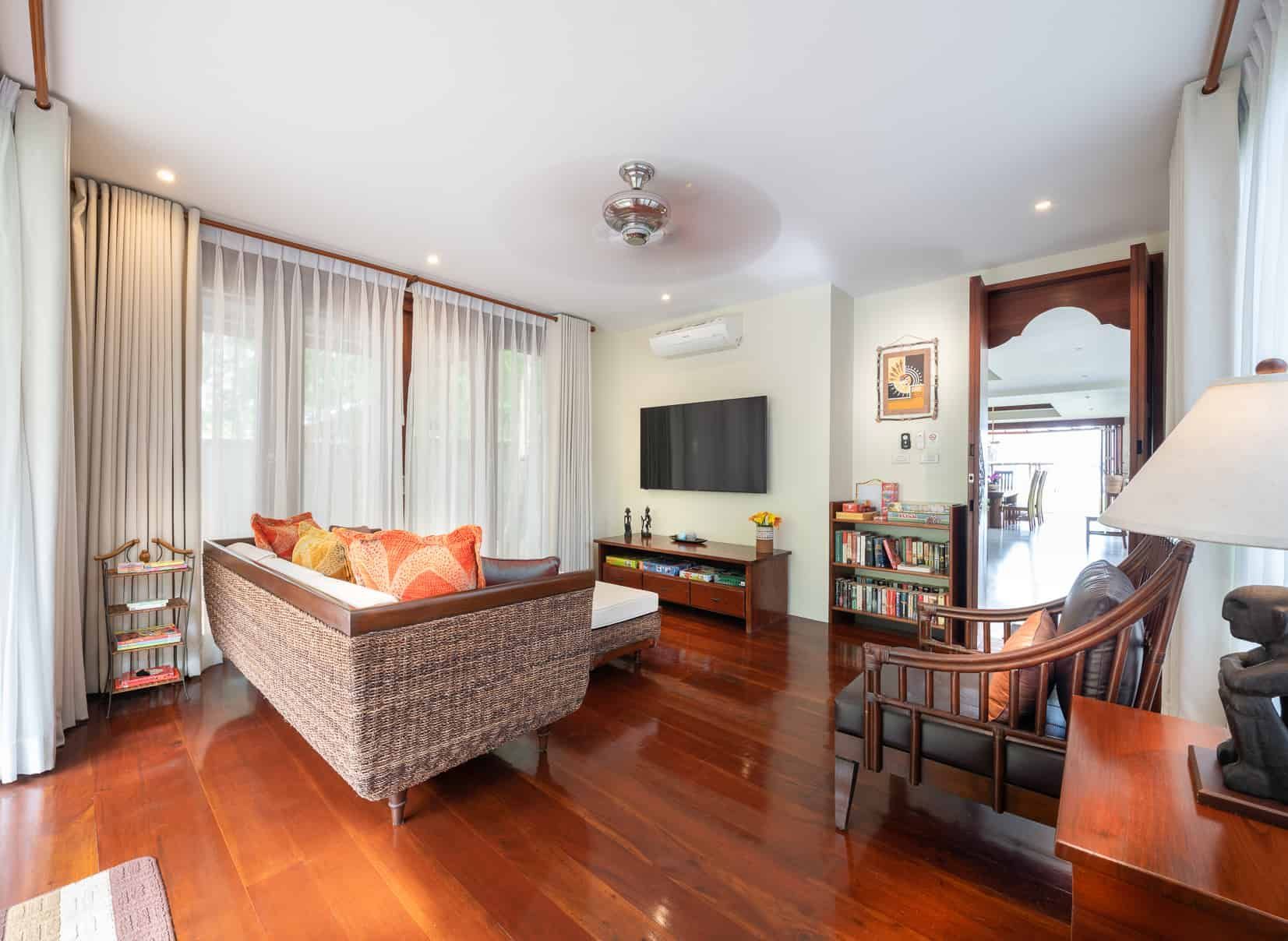 Living room with woven sofa, hardwood floors, and large windows with white curtains.