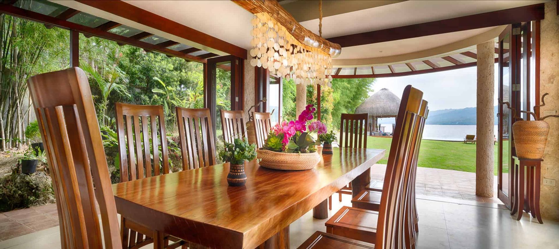 Dining area with wooden table and chairs, overlooking a lake and lush greenery.