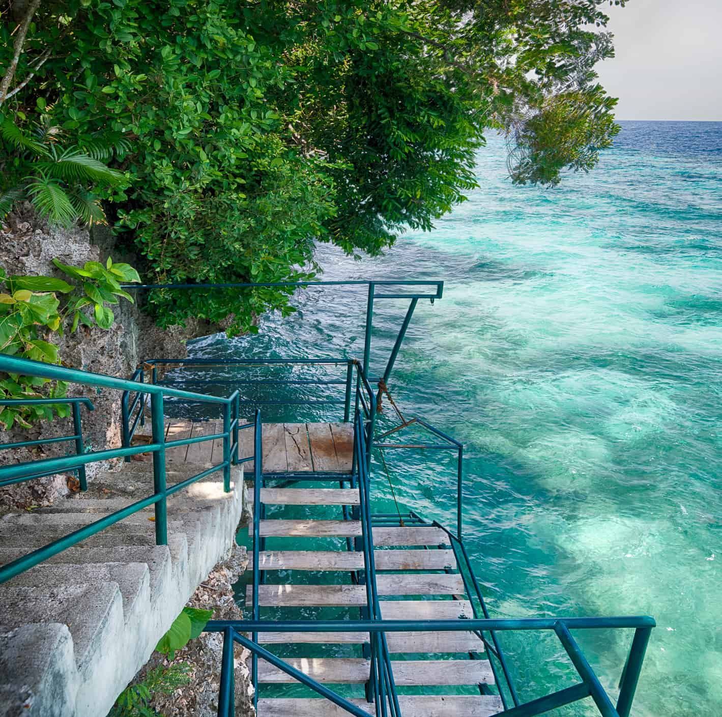 Staircase leading down to turquoise water, with lush green foliage overhead.